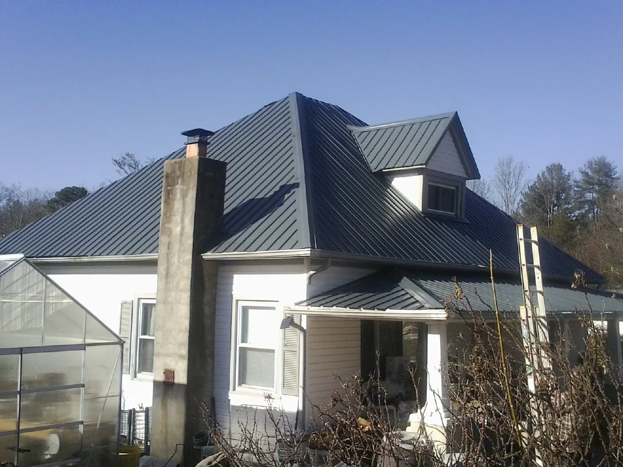 Dark blue standing seam metal roof on a white farmhouse with dormer — Slate & Tile Roof Repair by Roofing Brothers in Frederica