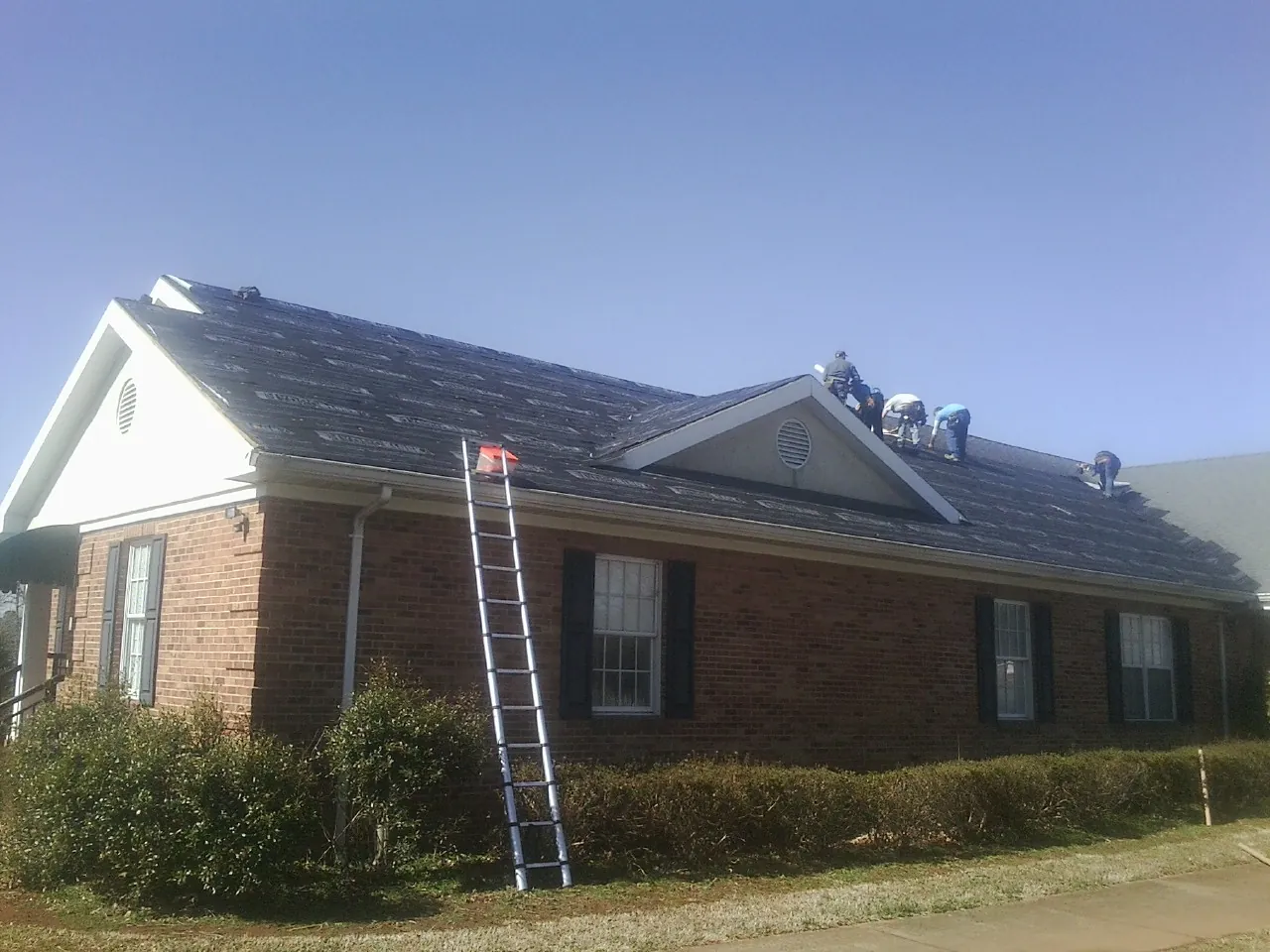 Crew tearing shingles off a brick ranch roof with a ladder set — Emergency Roof Repair work by our crew in Frederica