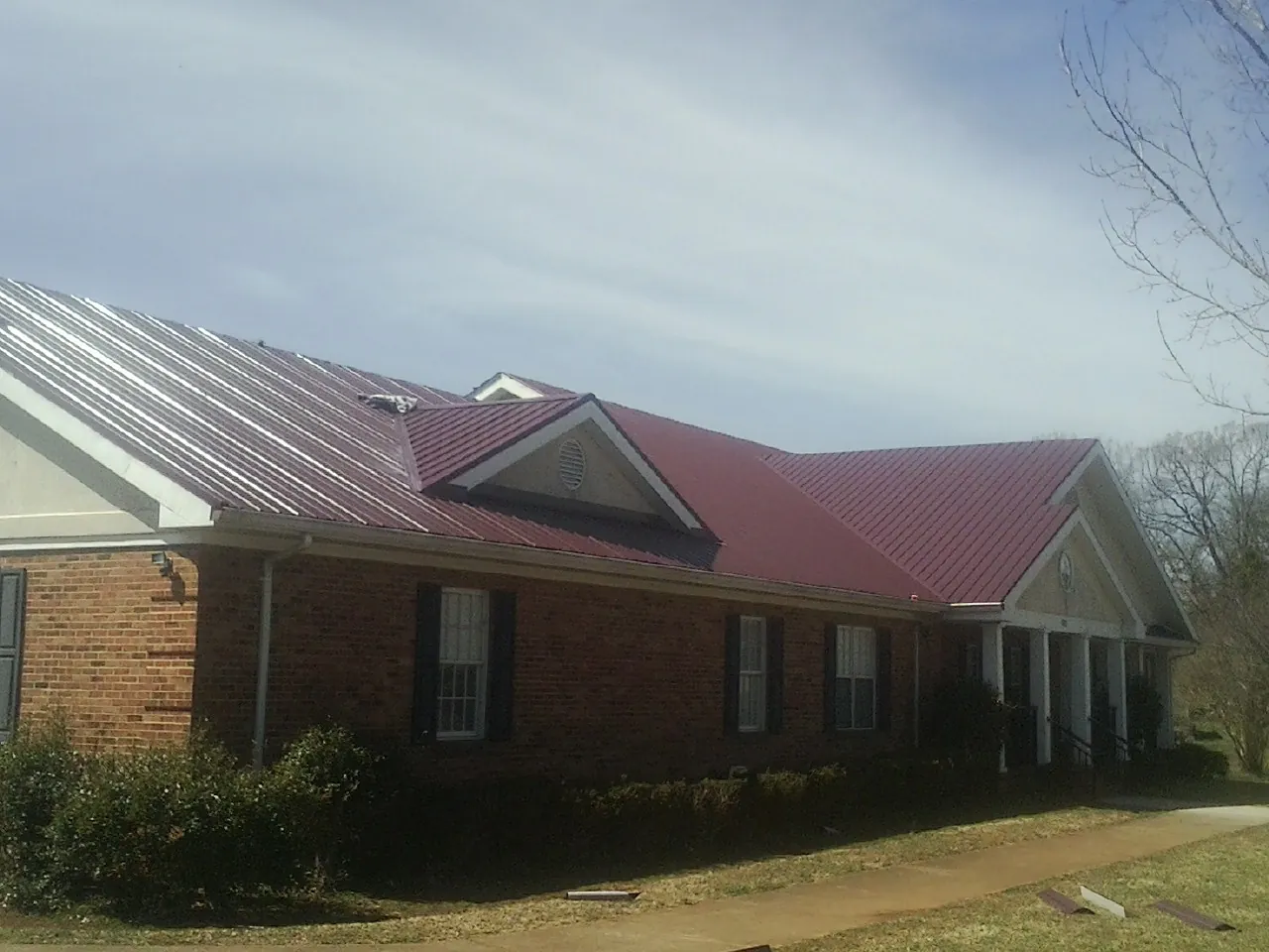 Red metal roof with gabled entries on a long brick building, from a Hail Damage Roof Repair job in Frederica