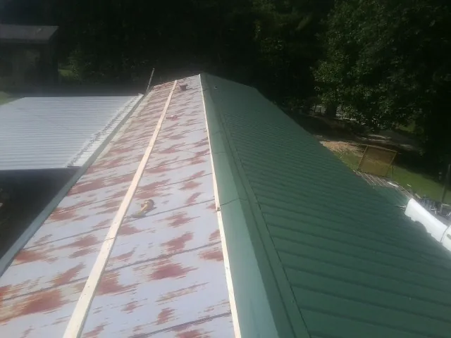 Old rusted panels beside newly installed green metal roofing — Wind Damage Roof Repair by Roofing Brothers in Frederica