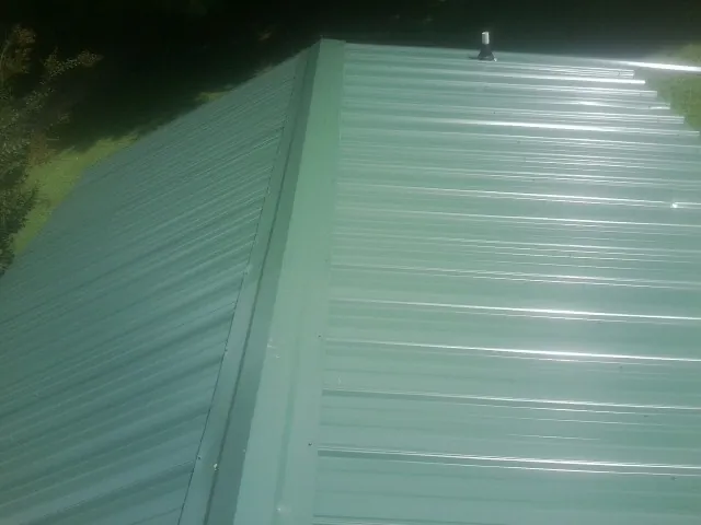 New green metal panels meeting at the ridge of a roof — Flat Roof Repair work by our crew in Frederica