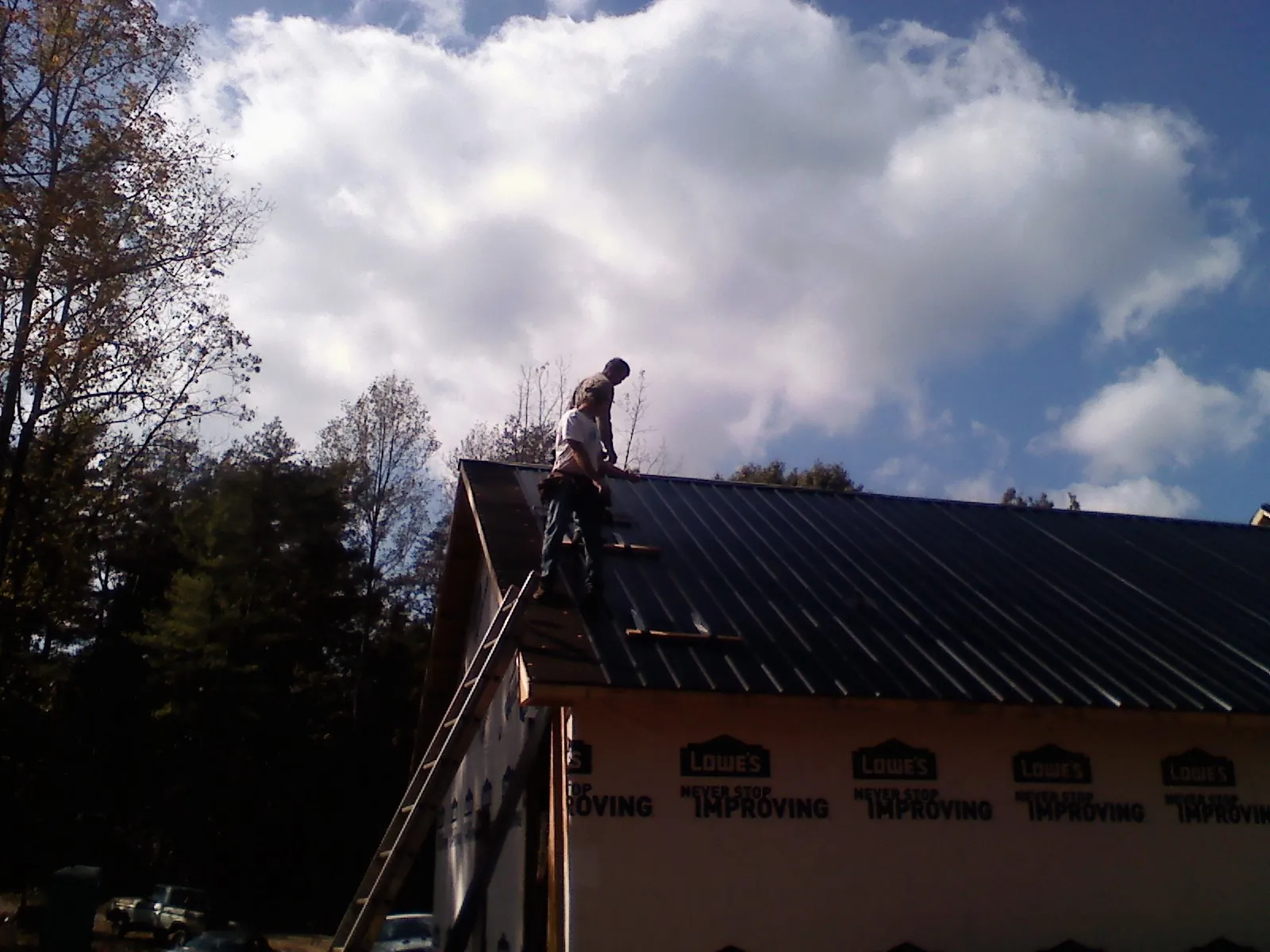 Roofer fastening dark metal panels high against a cloudy sky, from a Roof Inspection job in Frederica