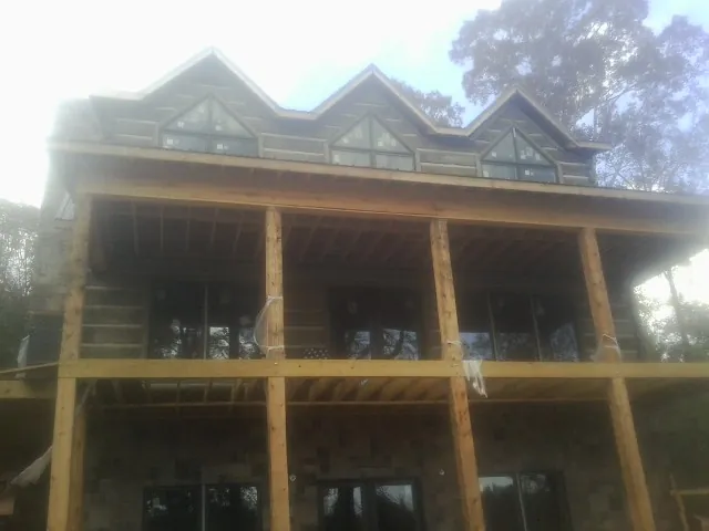 Dormers and porch framing on a large log home under construction — Roof Coating work by our crew in Frederica